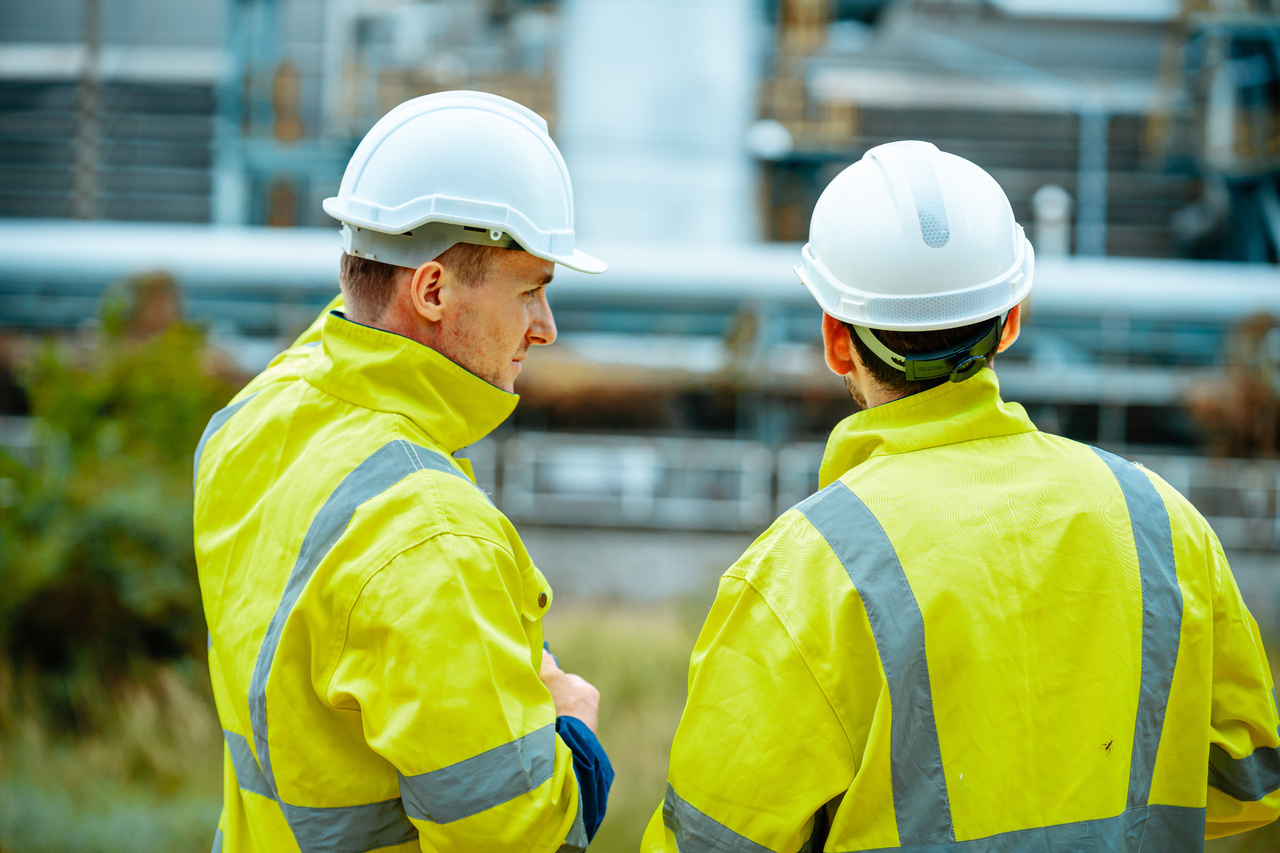Safety professional in a hard hat and hi-vis vest reviewing a tablet
